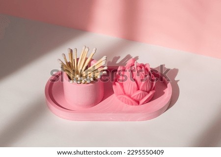A lotus candle and a glass with matches on a white-pink background.