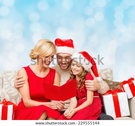 christmas, holidays,  family and people concept - happy mother, father and little girl in santa helper hats with gift boxes reading geeting card over blue lights background