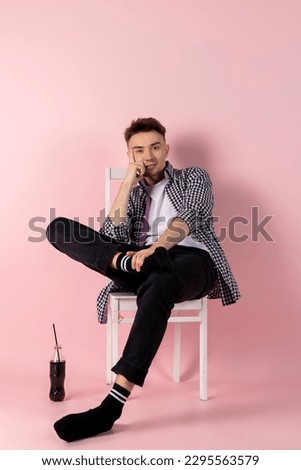 A happy young man sitting with a bottle of coke. fast food and sugar addiction. Isolated on pink background.