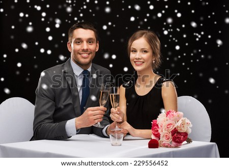 celebration, christmas, holidays and people concept - smiling couple clinking glasses of sparkling wine at restaurant over black snowy background