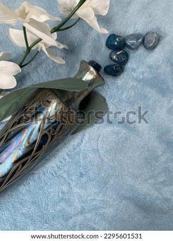 This unique photo captures an intriguing composition of elements, featuring a blue background, blue stones, a vibrant orchid, and a beautiful gradient vase, all laid out on the floor.