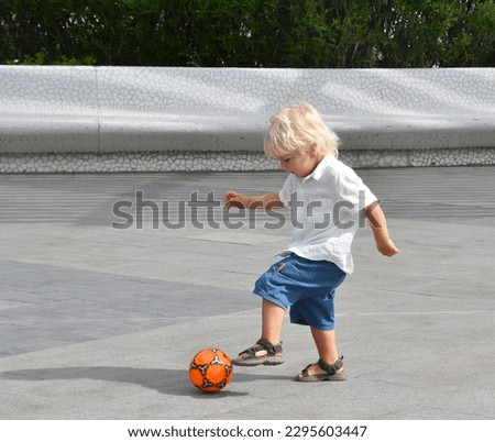 Little boy playing football on the empty square.. Active child in summer with ball Royalty-Free Stock Photo #2295603447