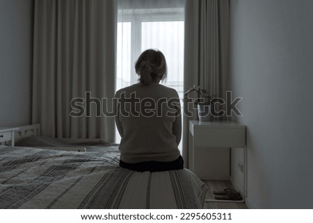 Mature woman sitting alone in the room, sad depressed person. Back view. mental health Royalty-Free Stock Photo #2295605311
