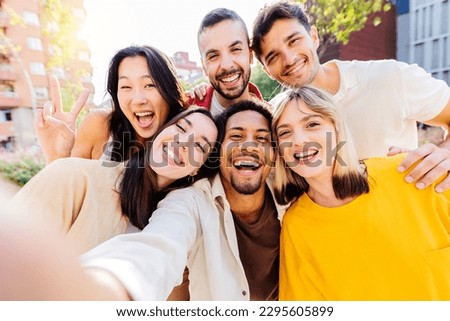 Happy group of diverse millennial friends taking selfie portrait together using mobile phone app. Multi ethnic teenage people having fun in city street. Friendship and youth lifestyle concept