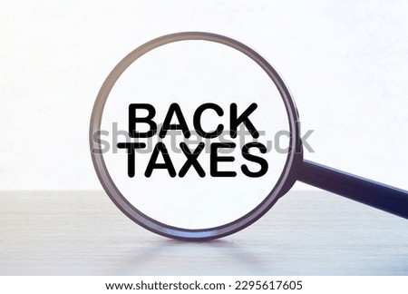 Magnifying glass with text BACK TAXES on wooden table.