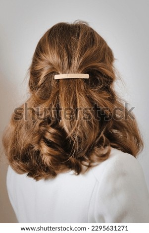 Young woman with thick, natural blonde hair pulled back and pinned half-up by a barrette hair clip. Gold metal barrette. Pretty hairstyle. Elegant hairstyle. Winter white coat. Cool vintage filter.  Royalty-Free Stock Photo #2295631271