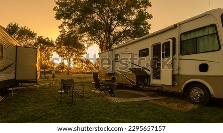 Sunset at campsite with trailer and motorhome on grass Royalty-Free Stock Photo #2295657157