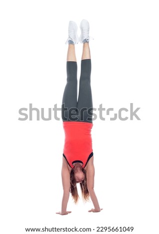 A young woman in sportswear stands on her hands. Gymnastics, sports acrobatics and yoga. Activity and health. Full height. Isolated on a white background. Vertical.