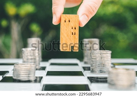 Hand choosing mini wood house and row of coin money on wood table, selective focus, Planning to buy property. Choose what's the best. A symbol for construction ,ecology, loan concepts	
