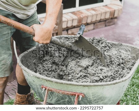 Man mixing concrete with shovel in wheelbarrow by hand Royalty-Free Stock Photo #2295722757