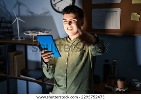 Non binary person using touchpad device at night approving doing positive gesture with hand, thumbs up smiling and happy for success. winner gesture. 