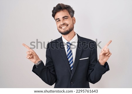 Young hispanic man with tattoos wearing business suit and tie smiling confident pointing with fingers to different directions. copy space for advertisement 