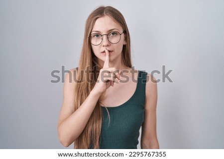 Young caucasian woman standing over white background asking to be quiet with finger on lips. silence and secret concept. 