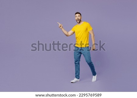 Full body side view young smiling confident caucasian man wear yellow t-shirt walking going point finger aside isolated on plain pastel light purple color background studio portrait. Lifestyle concept Royalty-Free Stock Photo #2295769589