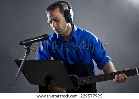 male singer holding a guitar and wearing headphones on concrete background