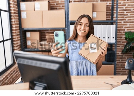Young beautiful hispanic woman ecommerce business worker holding package make selfie by smartphone at office