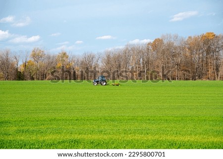 Working tractor with rotary cutters shredders on farmland meadow field, colorful fall foliage, cloud blue sky South Lockport, Niagara County, Upstate New York, USA. Agriculture industrial background