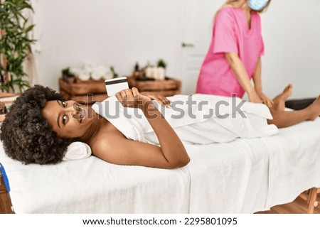 Young african american woman holding credit card having legs massage at beauty center