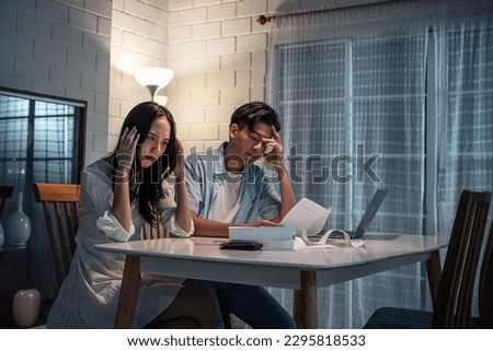 Asian young depressed couple having argument while checking money debt. Attractive new marriage man and woman looking frustrated to paperwork and bill, feel worried about financial problem in house. Royalty-Free Stock Photo #2295818533