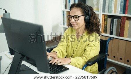 Middle age hispanic woman teacher using computer sitting on wheelchair at library university