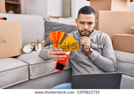 Young latin man using laptop holding test color at new home