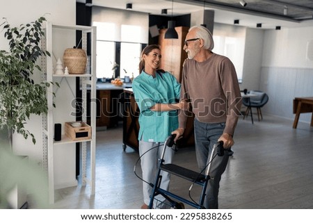 Caring young home care physiotherapist satisfied with recovery progress of elderly person with mobility walker supporting and cheering him up during home visit. Home care worker assisting old man. Royalty-Free Stock Photo #2295838265