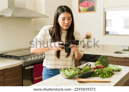 Caucasian influencer woman taking pictures of organic green vegetables and fruits before cooking a vegan recipe dish 