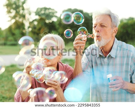 Happy active senior couple having fun blowing soap bubbles in park outdoors. Vitality and active senior couple concept Royalty-Free Stock Photo #2295843355