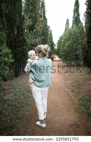 Rear view of a mother hugging her infant daughter on the street during the day. Walk in the woods in spring or autumn. Family look of mother and daughter. Mothers Day, child care, maternity leave