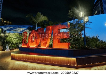 The "Love" sign is red with yellow lights shining at night. This sign is located above the "Love on Top" bridge located at Pondok Indah Mall (PIM) 3.