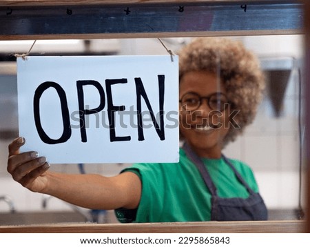 Sign that says open in a restaurant with an owner or waitress in the background out of focus