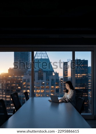 Young busy Asian business woman executive working on laptop at night in dark corporate office. Professional businesswoman manager using computer sitting at table, big city view from window. Vertical Royalty-Free Stock Photo #2295886615