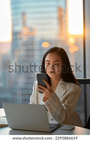 Young busy serious Asian business woman leader holding cellphone device using mobile phone, looking at smartphone checking financial market app working in modern corporate office, vertical. Royalty-Free Stock Photo #2295886619
