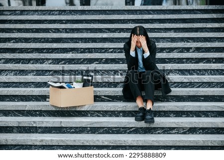 A visual representation of job loss and worklessness, as the woman sits on stairs, holding a cardboard box. Desperate Woman Sitting Alone Outdoors Royalty-Free Stock Photo #2295888809