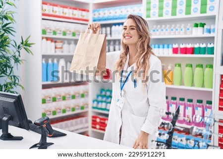 Young blonde woman pharmacist smiling confident holding shopping bag at pharmacy Royalty-Free Stock Photo #2295912291