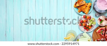 Refreshing summer food side border. Selection of grilled fruits, ice cream and ice pops. Top view on a blue wood banner background.