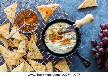 Baked brie cheese in a cast iron pan with pita triangles and red pepper jelly. Royalty-Free Stock Photo #2295919927