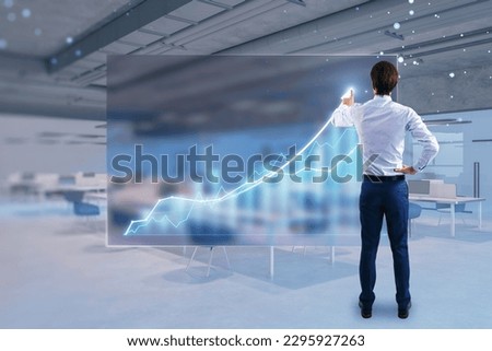 Back view of young businessman using abstract growing business chart hologram on blurry office interior background. Trade, finance and investment concept. Double exposure