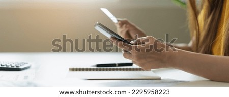 Close up view hands of young woman holding a credit card and doing bank transactions via mobile phone application at home