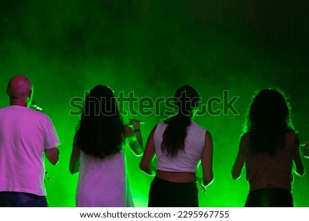 Group of people rehearsing and singing in empty theater seen from the stage, with green light in the background