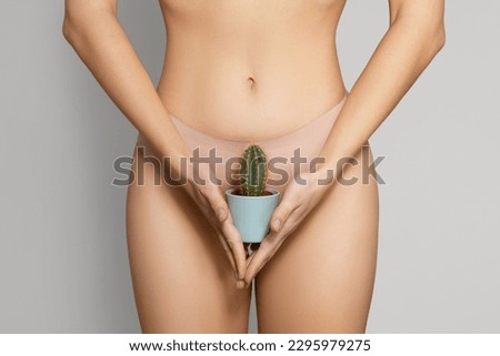 Young woman holing cactus in pot standing in beige panties over grey studio background, closeup, cropped. Epilation, intimate hygiene, hair removal and smoothness concept