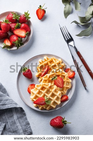 Homemade soft waffles with fresh strawberries in a plate on a light background. Traditional Belgian waffles. Healthy vegetarian breakfast. Top view. Royalty-Free Stock Photo #2295983903