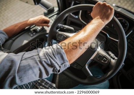 Truckers Hand on a Semi Truck Steering Wheel Close Up Photo. Caucasian Professional Driver Theme. Transportation Industry. Royalty-Free Stock Photo #2296000069