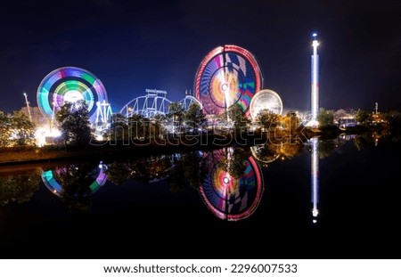 night view longtime exposure of the fairground Stuttgarter Wasn in Stuttgart. Reflection of ferris wheels  in water of the river Neckar. Colorful light effects Royalty-Free Stock Photo #2296007533