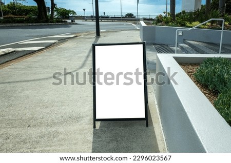 Empty blank white street advertising sandwich board mockup template displayed outdoors on the walkway of a street near a roundabout. Background texture of mobile easel board with copy space for text.