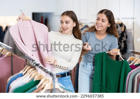 Happy female friends choosing between green and pink cardigans in a clothing store