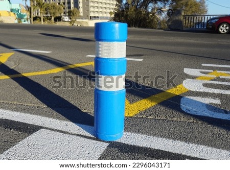 Blue and white road limiting column on the grey asphalt with white and yellow lines 