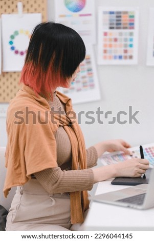 Creative young graphic designer choosing a color from the sampler and drawing on a digital tablet computer at workplace