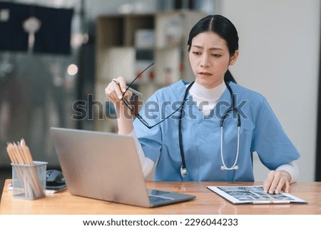 Professional millennial female doctor or nurse working on laptop computer and clipboard with a tense expression while sitting at a desk