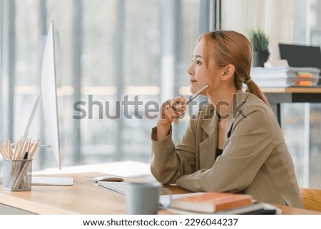 A focused and professional millennial Asian graphic designer, woman working on computer and deep in thought at modern office